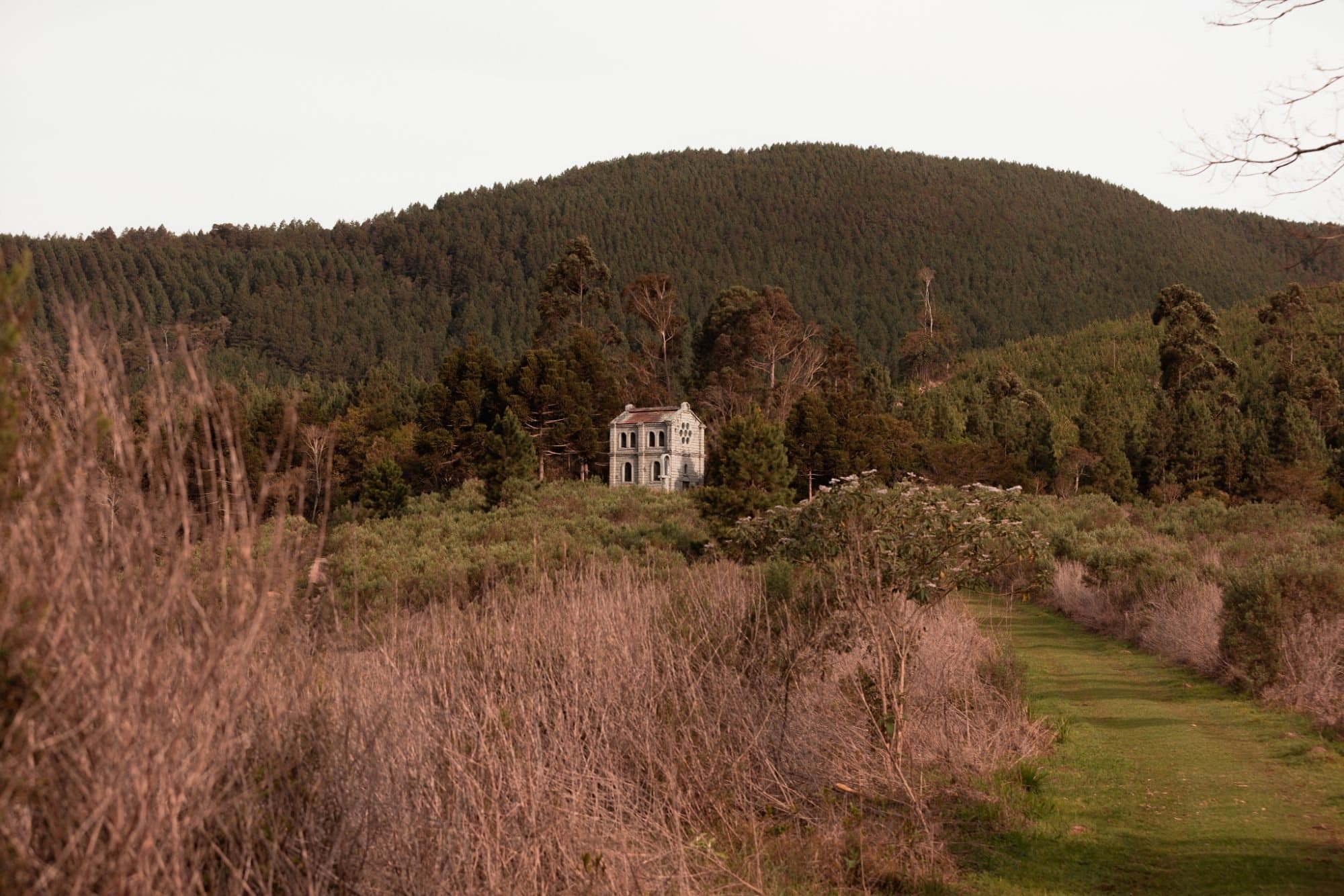 Campo e mata com uma casinha de pedra ao fundo
