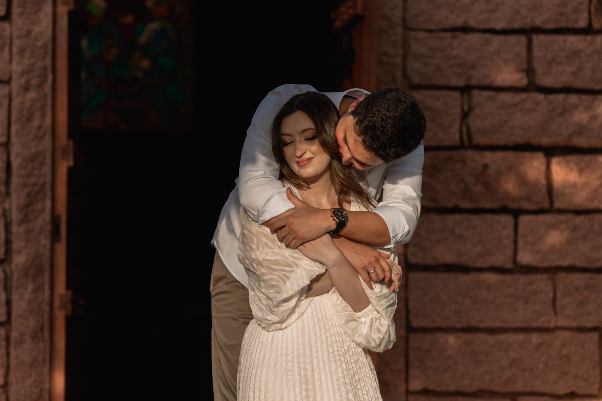 Maria Eduarda e João Guilherme abraçados em frente a uma capela de pedra